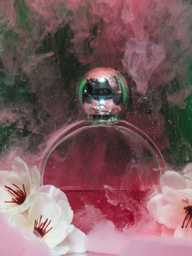 A vertical shot of a bottle of perfume with pink powder and flowers against a dark background