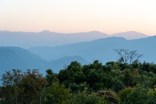 A breathtaking sunset over a rolling landscape of hills and lush green trees in the foreground