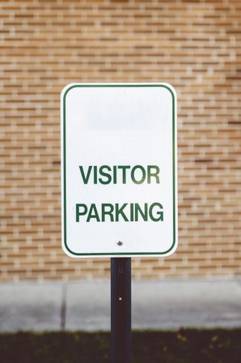 A vertical shot of a sign for visitor parking on the brick wall background