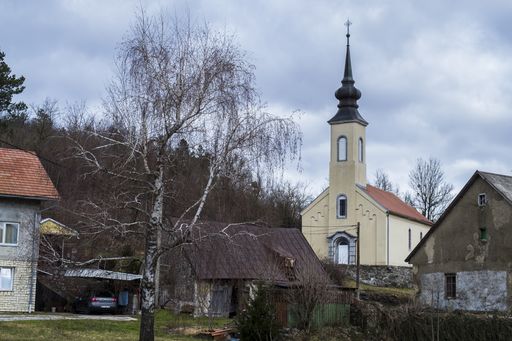 A church surrounded by hills covered in greenery and houses under a cloudy sky