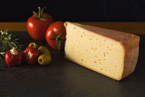 A piece of  German cheese Tilsiter with tomato and olives on a black slate