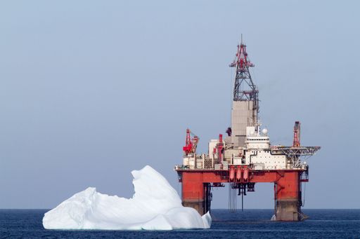 An offshore oil rig on the surface of blue water in the ocean with a floating iceberg.