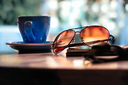 A closeup moody bokeh shot of aviator type of glasses with a blue cup of coffee with a blurred background