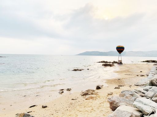 A scenic beachfront view with a rocky coastline and an air balloon in the background