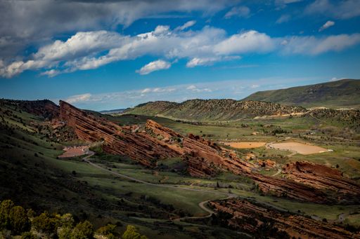 A scenic view of rolling green hills surrounded by tall pine trees against a cloudy blue sky