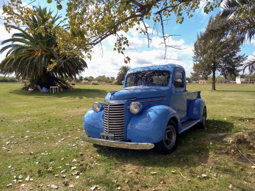 Old blue 1940 Chevrolet Chevy pickup truck hot rod in the countryside under a tree. CAACMACH 2023 classic car show. Sunny day