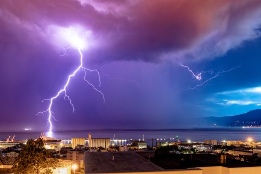 The lightnings striking on the ocean from gloomy skies at night framed with coastal buildings