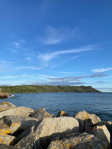 A vertical shot of a coastline featuring large rocks with waves crashing against them near the shoreline