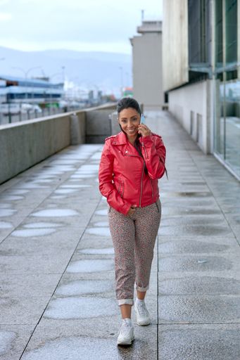 A vertical shot of a Hispanic female in a leather jacket talking on her phone on the street