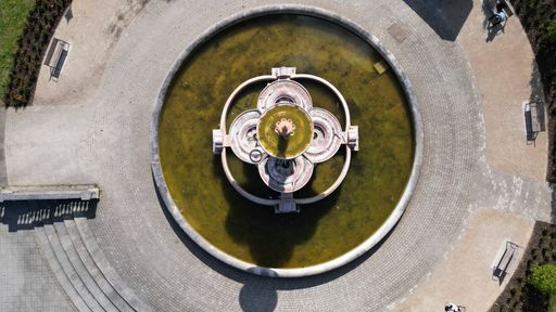 An aerial shot of a circular fountain in the park on a sunny day