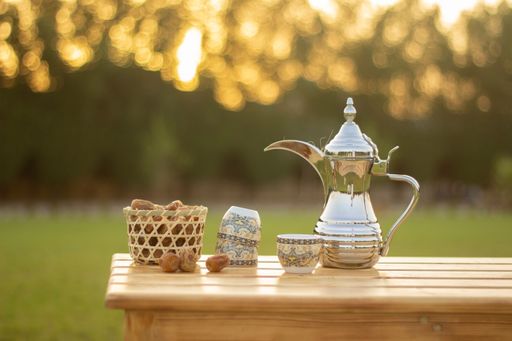 A silver teapot on a wooden table with cups and dried apple on a grassy lawn in a sunny outdoor setting