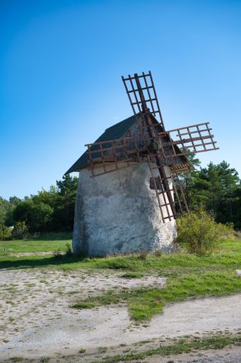 A rustic windmill set against a backdrop of a picturesque field with a dirt path meandering through it