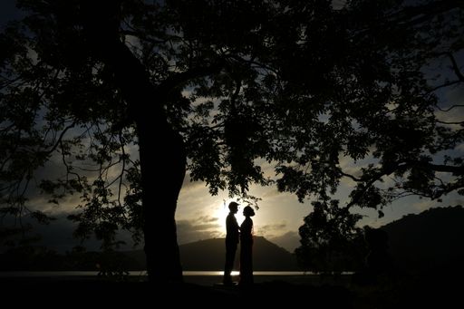 A silhouette of couple standing near lake and holding friends during sunset