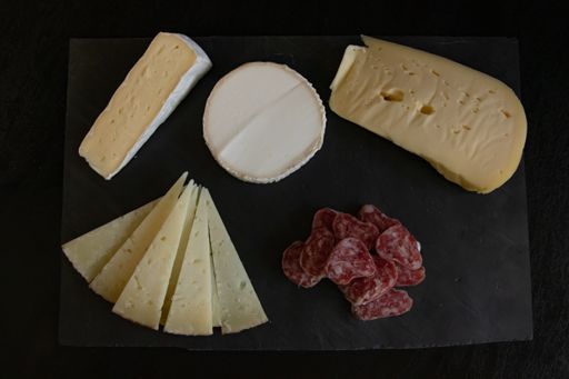 A high angle shot of different kinds of cheese and salami on a black surface