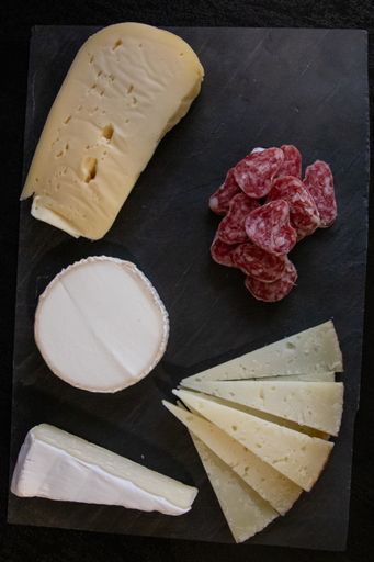 A vertical shot of different kinds of cheese and salami on a black surface