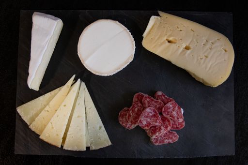 A high angle shot of different kinds of cheese and salami on a black surface