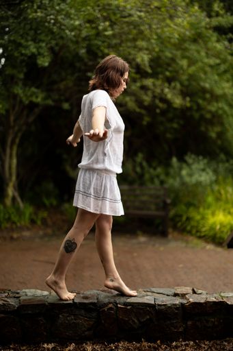 A female walking over a stone fence in a picturesque outdoor environment