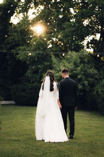 A newlywed couple walking hand in hand through a lush field at sunset.