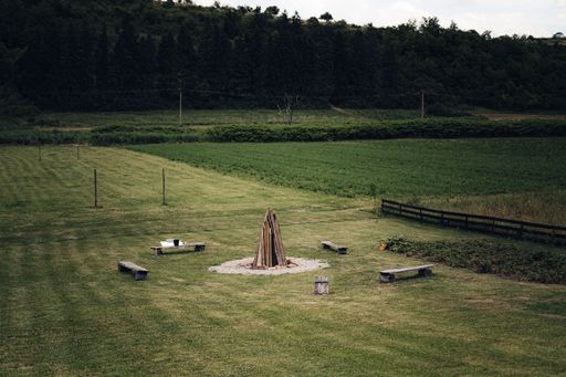 An outdoor scene of a grassy field with benches arranged around a fire pit