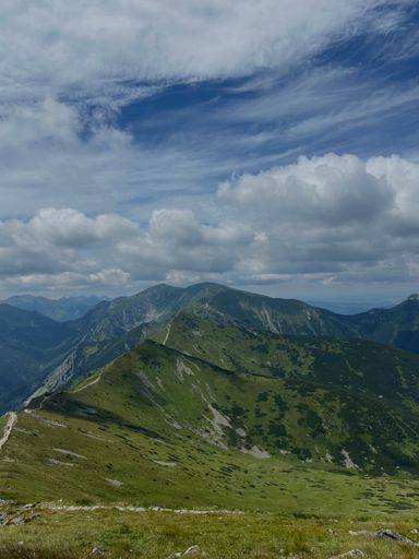 A landscape view of the green mountains and peaks against a clouded blue sky