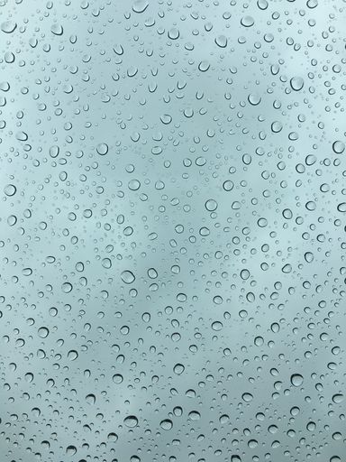 A close up of a windowpane with a glass surface, featuring a wet, gray backdrop with droplets of water scattered across the pane