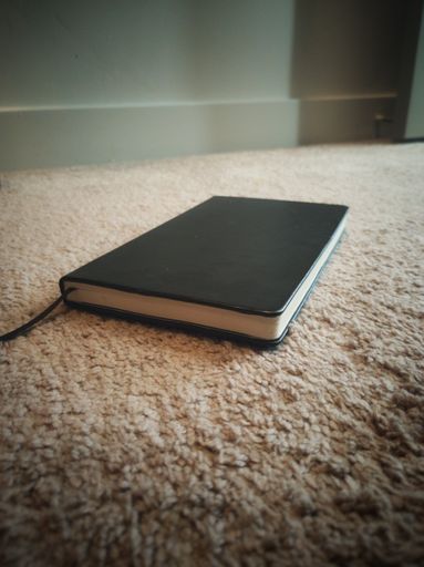 A black notebook on the floor with a soft carpet