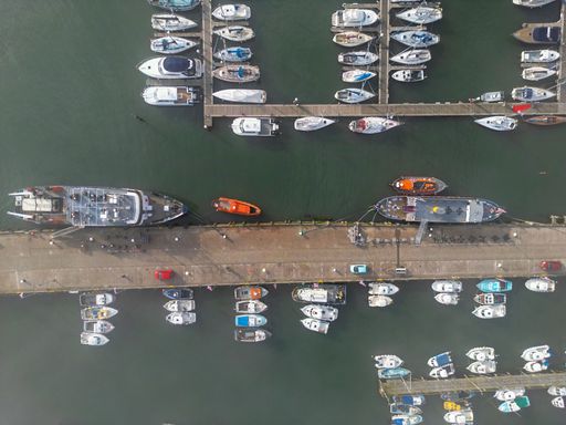 An aerial view of a bustling marina with a variety of boats of various sizes lined up side-by-sids