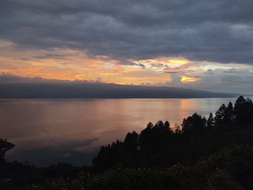 A beautiful view of the lake surrounded by nature under a cloudy sunset sky