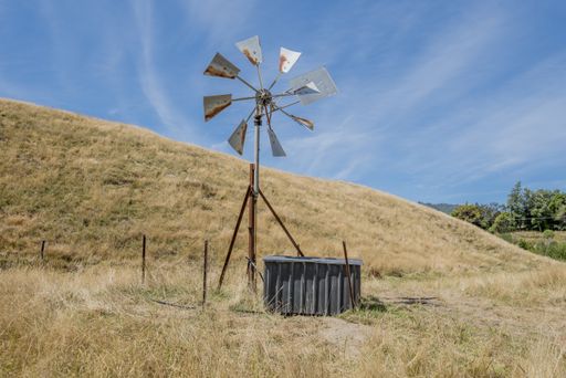 A rustic small farm windmill used for pumping water in a rural setting, the little pump house is alongside