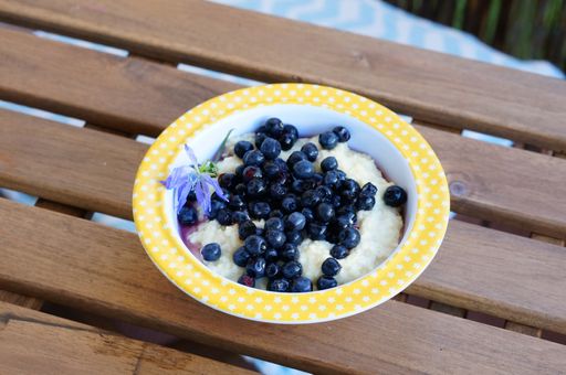 A closeup shot of a bowl of semolina topped with blueberries  on a wooden table