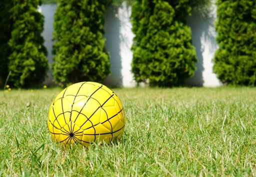 A closeup shot of a yellow soccer ball on a grassy field with greenery in the background