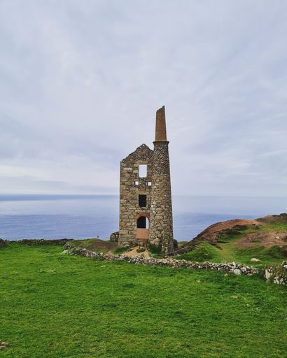 An aged brick tower stands tall atop a hill, providing a magnificent view of the vast ocean beneath: Mines in Cornwall