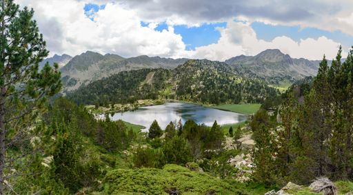 A lake surrounded by rocks and hills covered in greenery under a cloudy sky and sunlight