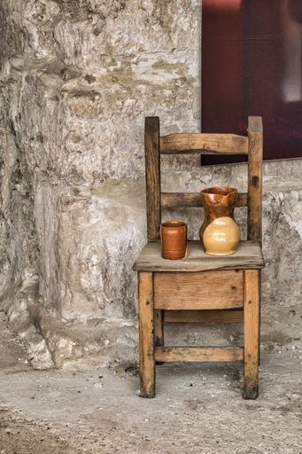 A vertical shot of an antique wooden chair with two clay jugs for serving wine