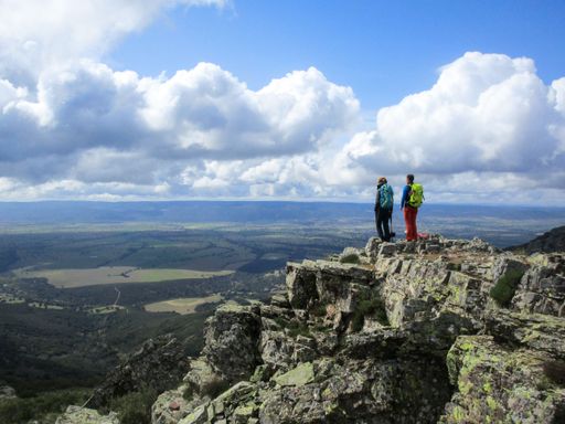 A hiker couple on top of a rocky mountain with their dog enjoying the scenic view