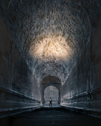 A person making their way through a dimly lit urban tunnel