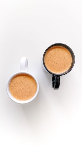 A top view of white and black cups of chai tea on a white minimal background