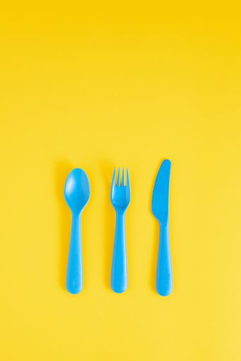 A top view of blue plastic spoon, fork and knife on a yellow pastel background with copy space above