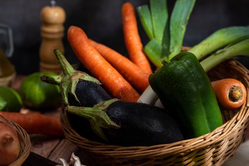 A wicker basket filled with a variety of fresh, colorful vegetables sits atop a rustic wooden table