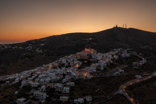 A vibrant cityscape on a hilltop illuminated by the golden rays of an ethereal sunset near Syros Island