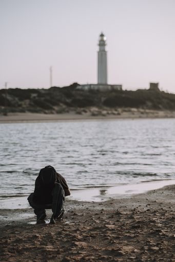 A man at the shore near the Cape Trafalgar lighthouse on a gloomy day