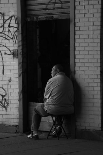 A grayscale shot of a man sitting in a chair in front of a wall featuring a vibrant graffiti mural.