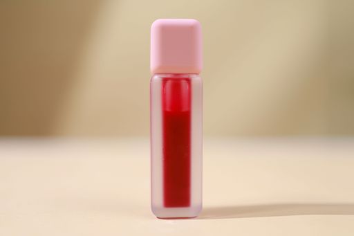 A close-up shot of a red lipstick encased in a gold-colored tube against a beige background