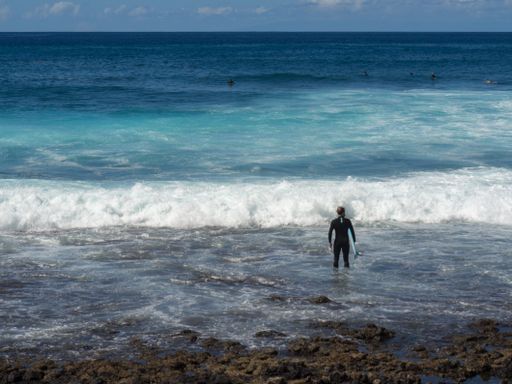 A surfer with his board standing at the shore looking at ocean waves