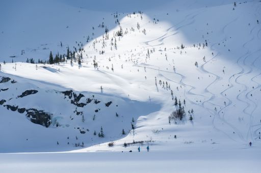 A vast expanse of a snow-covered field leading to the mountain with people climbing up