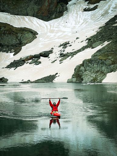 A person kayaking in a lake, surrounded by snowy mountains