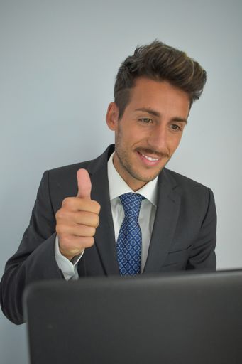 A smiling Spanish businessman in a suit showing thumbs in front of a laptop