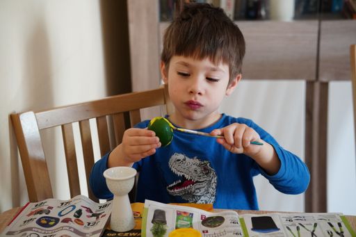 Young three years old Polish Caucasian boy painting a egg by a table to prepare for the traditional Easter holidays.