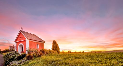 An idyllic rural landscape featuring a small chapel church surrounded by lush green grass illuminated by the golden evening light of beautiful sunset