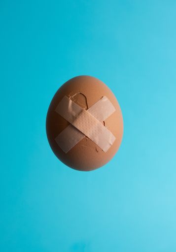 A vertical shot of a red cracked egg stitched by band aid cross on bright blue background with copy space